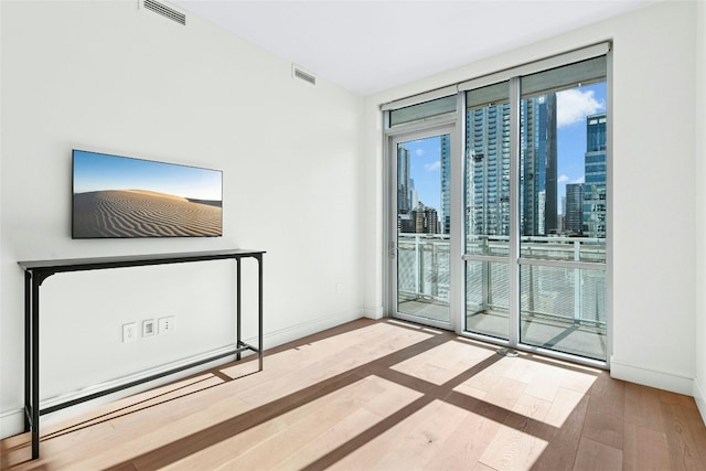 spare room with visible vents, baseboards, expansive windows, wood finished floors, and a view of city