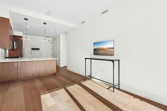 kitchen featuring light wood finished floors, stainless steel microwave, visible vents, pendant lighting, and a peninsula