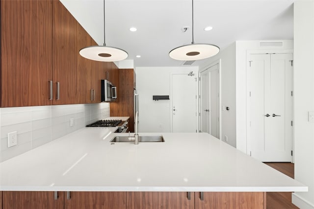 kitchen with stainless steel microwave, decorative light fixtures, light countertops, brown cabinets, and a peninsula