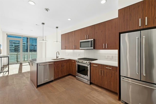 kitchen featuring light countertops, premium appliances, decorative backsplash, a peninsula, and a sink