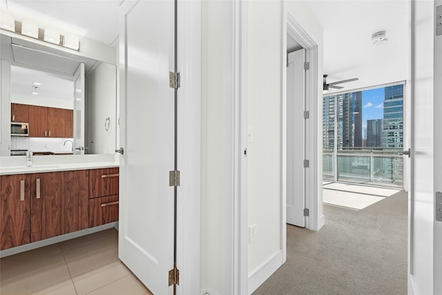 hall with a sink, expansive windows, light carpet, and light tile patterned floors