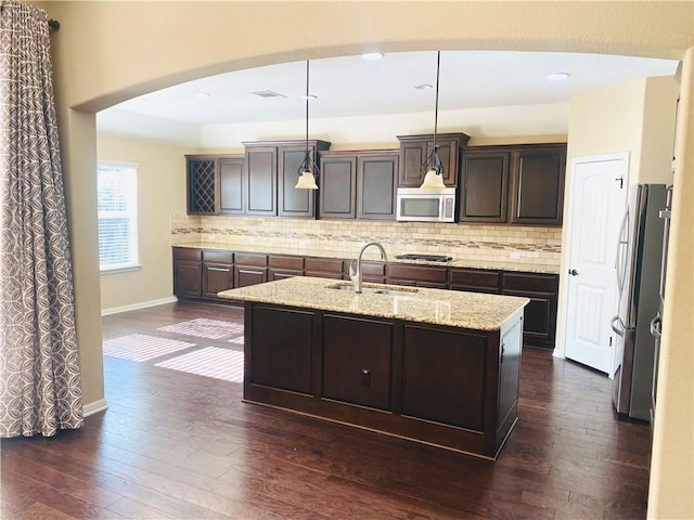 kitchen featuring tasteful backsplash, a sink, a center island with sink, stainless steel appliances, and dark wood-style flooring