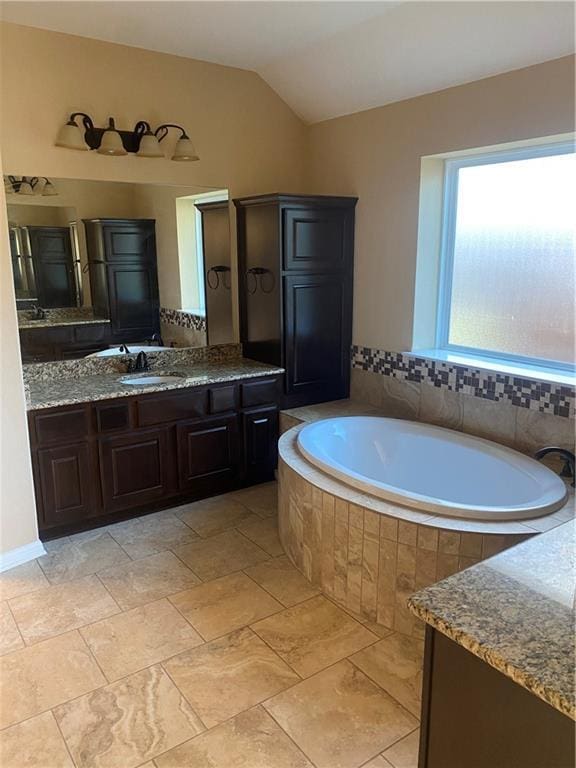 full bath with lofted ceiling, a bath, and vanity