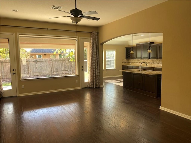 unfurnished living room featuring a sink, dark wood finished floors, arched walkways, and ceiling fan