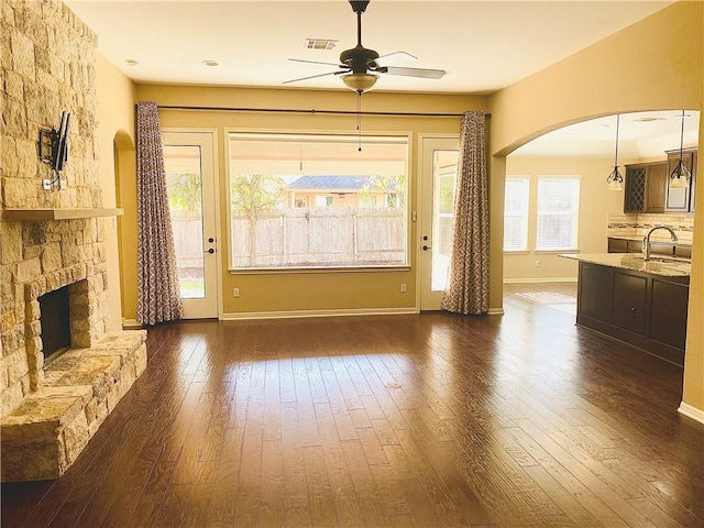 unfurnished living room featuring visible vents, a ceiling fan, a sink, arched walkways, and dark wood-style flooring