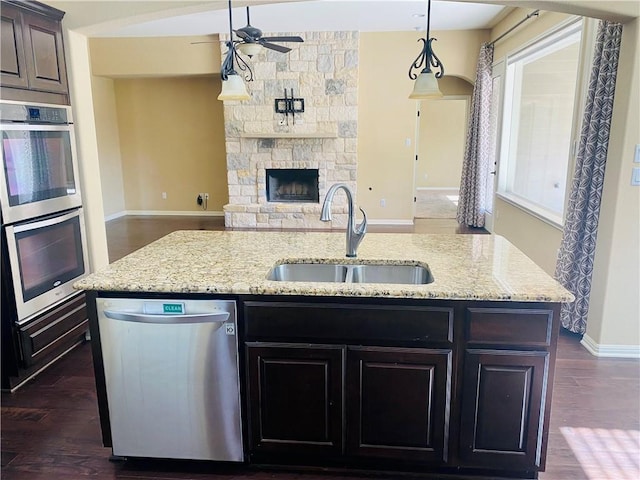 kitchen featuring open floor plan, a center island with sink, appliances with stainless steel finishes, a ceiling fan, and a sink