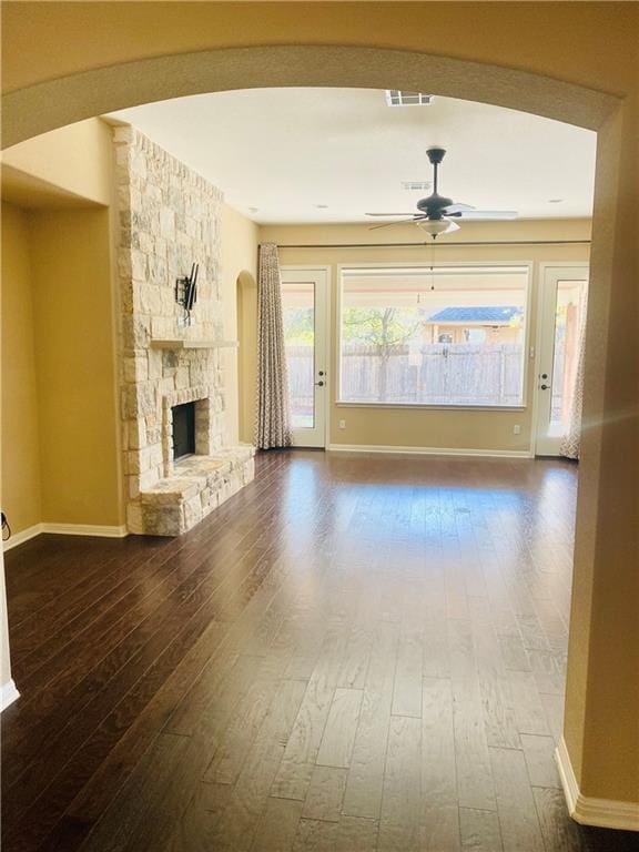 unfurnished living room featuring visible vents, a ceiling fan, a stone fireplace, baseboards, and dark wood-style flooring