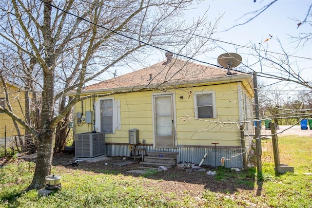 rear view of property with entry steps, central AC unit, and roof with shingles