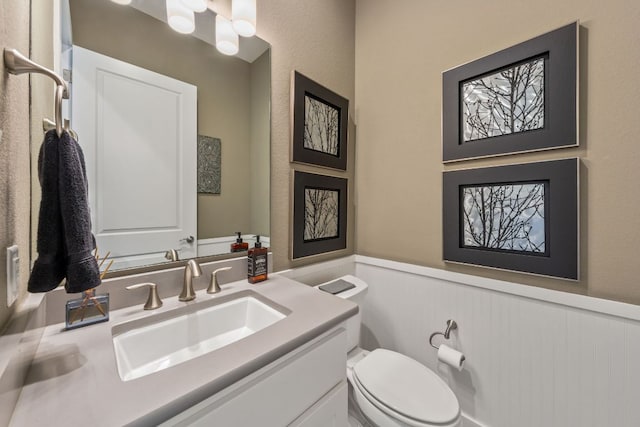 half bathroom with a wainscoted wall, toilet, and vanity