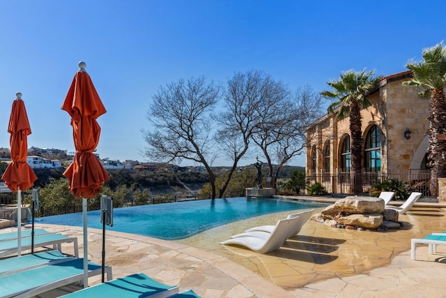 view of swimming pool with a patio area, an infinity pool, and fence