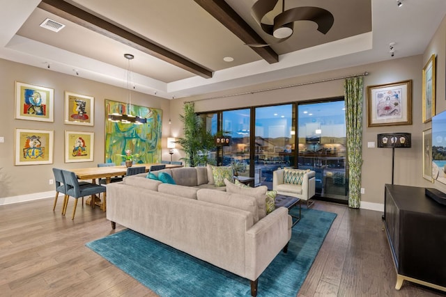 living area with baseboards, visible vents, hardwood / wood-style flooring, a raised ceiling, and a chandelier