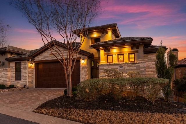 prairie-style home featuring a tile roof, an attached garage, stone siding, and driveway