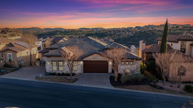 view of front of house featuring a tiled roof, an attached garage, stone siding, and driveway