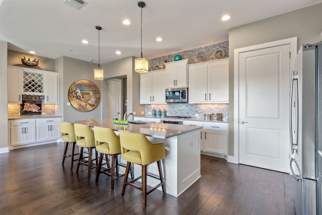 kitchen featuring white cabinets, appliances with stainless steel finishes, a breakfast bar, and dark wood-style flooring