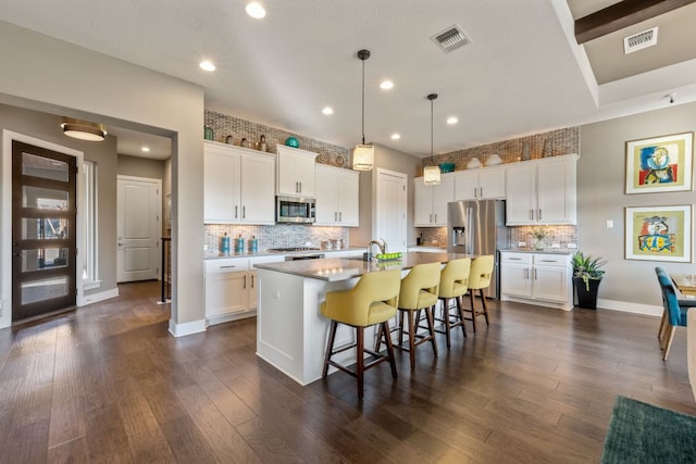 kitchen with visible vents, a breakfast bar area, an island with sink, appliances with stainless steel finishes, and dark wood-style flooring