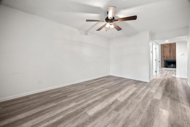 empty room with a ceiling fan, wood finished floors, baseboards, a fireplace with raised hearth, and a textured ceiling