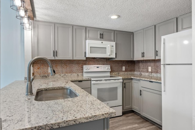 kitchen featuring white appliances, light stone countertops, gray cabinetry, a sink, and backsplash