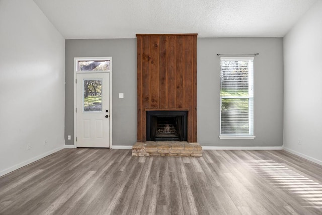 unfurnished living room featuring baseboards, a large fireplace, and wood finished floors