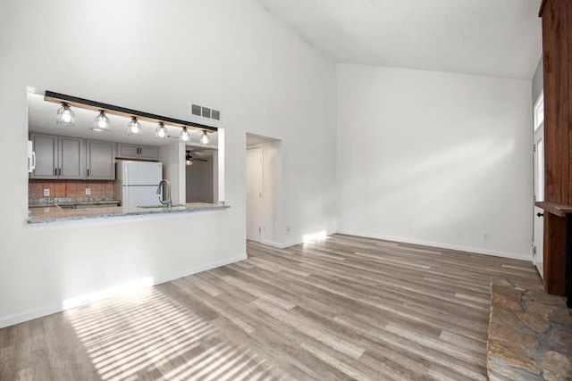 unfurnished living room featuring a sink, visible vents, baseboards, and wood finished floors