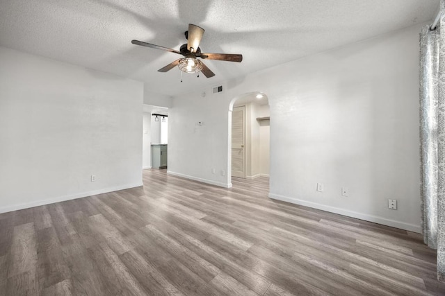 empty room with wood finished floors, visible vents, a ceiling fan, arched walkways, and a textured ceiling