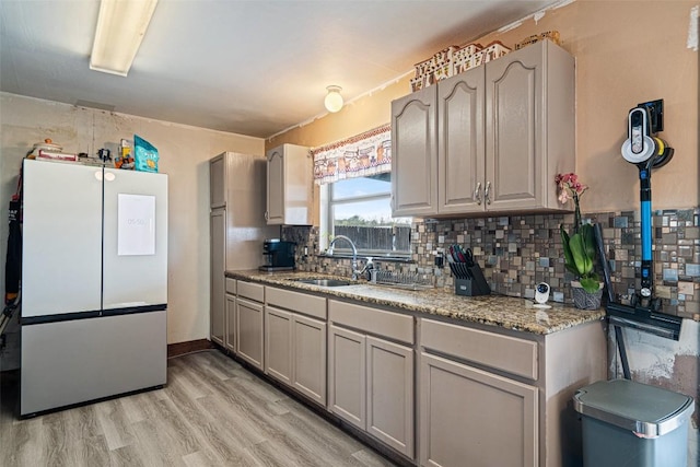 10505 Ruidosa St, Austin, TX 78719 - kitchen featuring backsplash, gray cabinetry, light wood-style flooring, freestanding refrigerator, and a sink