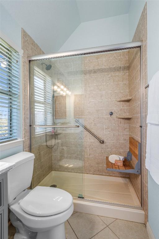 bathroom featuring toilet, a stall shower, tile patterned flooring, and vaulted ceiling