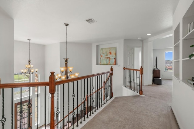 hall featuring visible vents, an upstairs landing, a chandelier, and carpet flooring