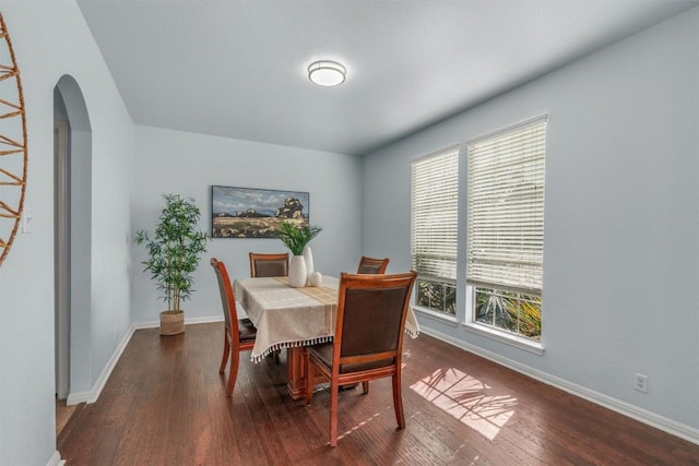 dining room featuring wood finished floors, arched walkways, and baseboards