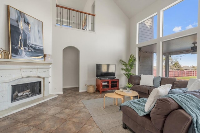 tiled living area featuring arched walkways, high vaulted ceiling, baseboards, and a high end fireplace