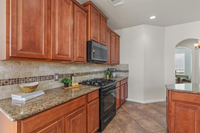 kitchen featuring visible vents, light stone counters, tasteful backsplash, arched walkways, and black gas range oven