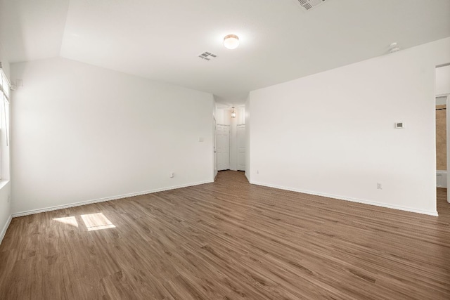 empty room featuring vaulted ceiling, visible vents, baseboards, and wood finished floors