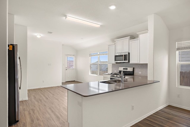 kitchen featuring a sink, tasteful backsplash, stainless steel appliances, light wood-style floors, and vaulted ceiling