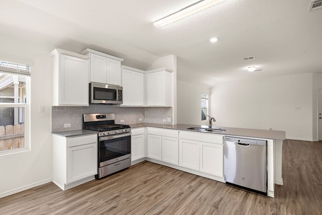 kitchen featuring a peninsula, a sink, light wood-style floors, appliances with stainless steel finishes, and backsplash