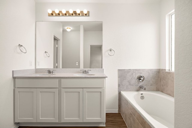 bathroom with a sink, a garden tub, wood finished floors, and double vanity