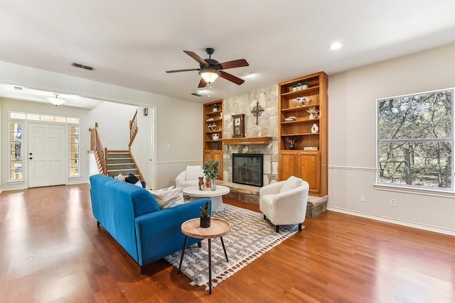 living area with visible vents, built in features, wood finished floors, a fireplace, and stairs