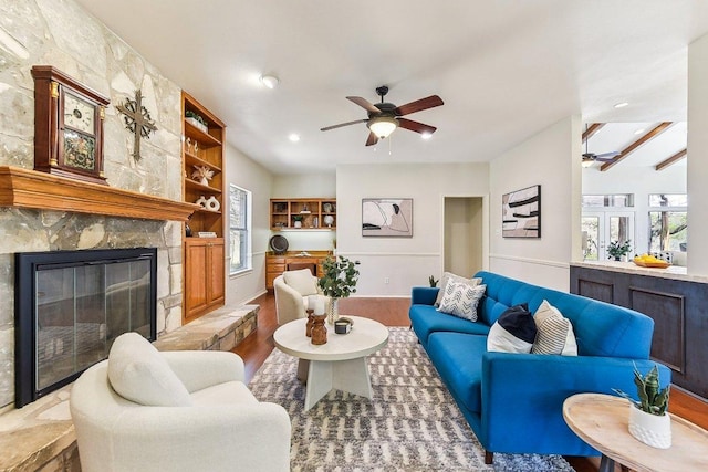 living area featuring a wealth of natural light, wood finished floors, a stone fireplace, and ceiling fan