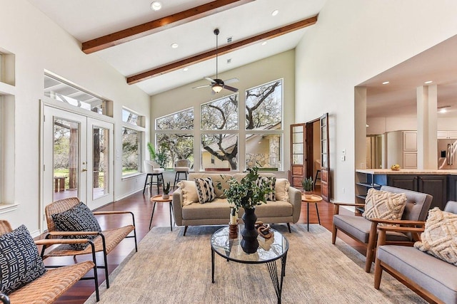 living room with beam ceiling, light wood-style flooring, a towering ceiling, french doors, and ceiling fan