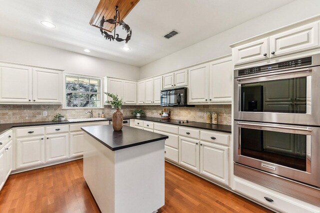 kitchen with dark countertops, visible vents, tasteful backsplash, black appliances, and a sink