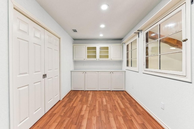 interior space featuring recessed lighting, light countertops, white cabinets, glass insert cabinets, and light wood-type flooring