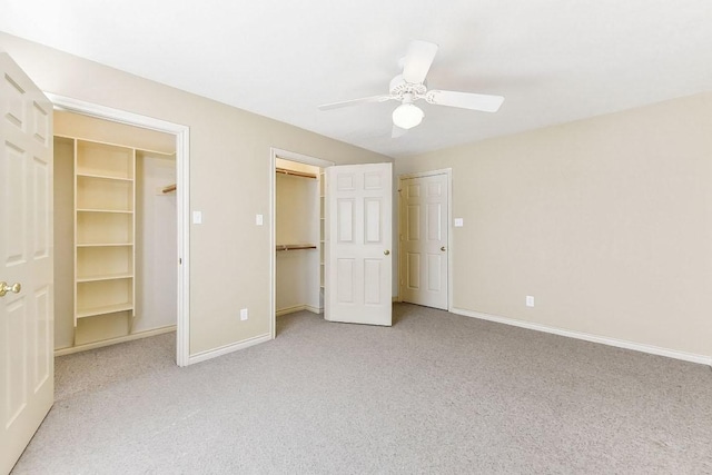 unfurnished bedroom featuring light colored carpet, a ceiling fan, a walk in closet, and baseboards