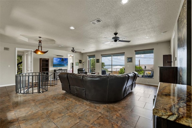 living room featuring a textured ceiling, baseboards, visible vents, and ceiling fan