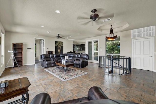 living room featuring baseboards, a ceiling fan, visible vents, and a textured ceiling