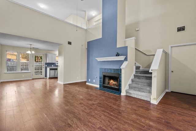 3609 Mims Cv, Austin, TX 78725 - unfurnished living room with a high ceiling, a tile fireplace, a chandelier, wood finished floors, and stairs