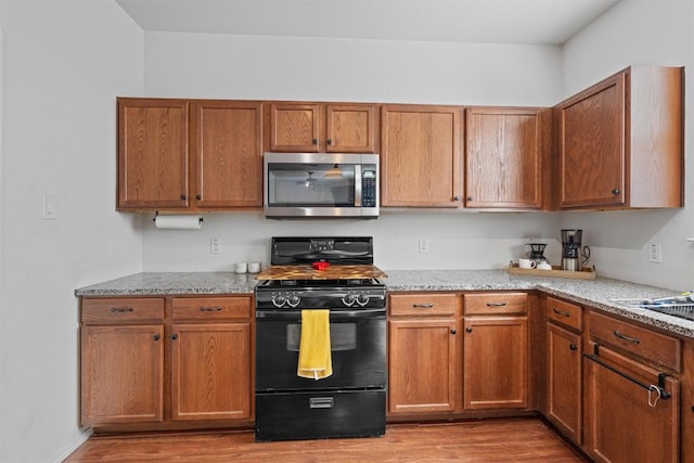 18037 Basket Flower Bnd, Elgin, TX 78621 - kitchen featuring stainless steel microwave, black range with gas stovetop, wood finished floors, and brown cabinets