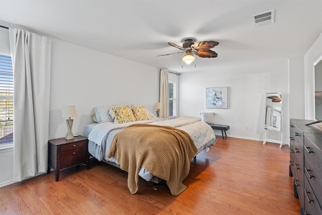 bedroom with light wood-style floors, visible vents, baseboards, and a ceiling fan