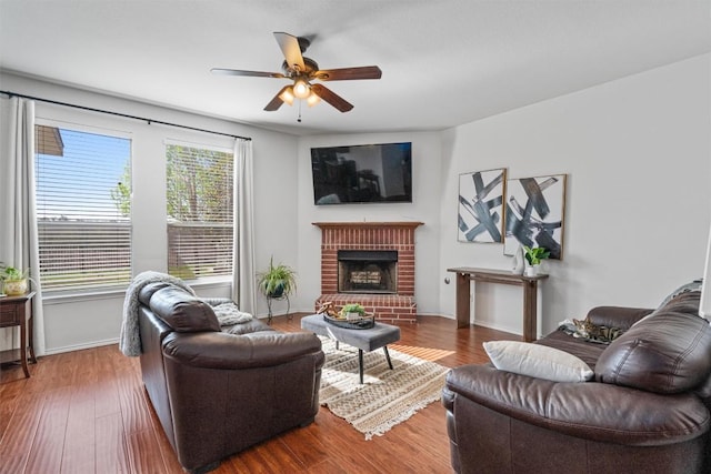 living area featuring ceiling fan, a brick fireplace, wood finished floors, and baseboards
