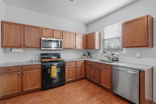 kitchen featuring a sink, light wood-style floors, brown cabinetry, stainless steel appliances, and light stone counters