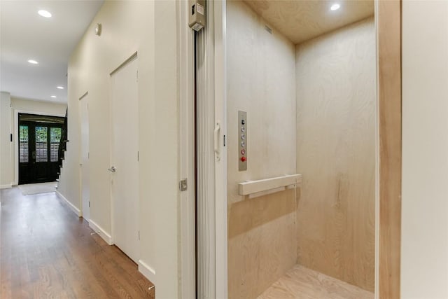 corridor featuring wood finished floors, elevator, recessed lighting, and baseboards