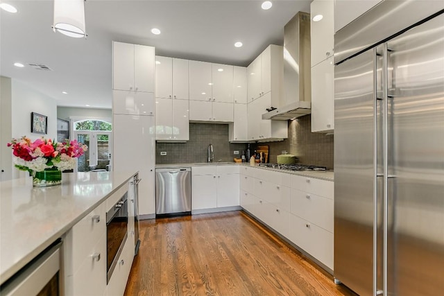 kitchen featuring visible vents, modern cabinets, a sink, appliances with stainless steel finishes, and wall chimney exhaust hood