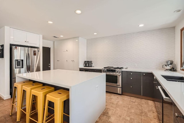 kitchen with a kitchen breakfast bar, a center island, appliances with stainless steel finishes, light countertops, and decorative backsplash